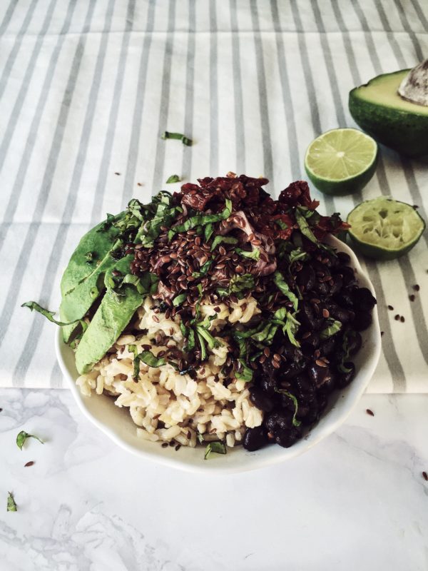 un buddha bowl vegetariano e caraibico: riso integrale, avocado, fagioli neri, coriandolo e semi di lino