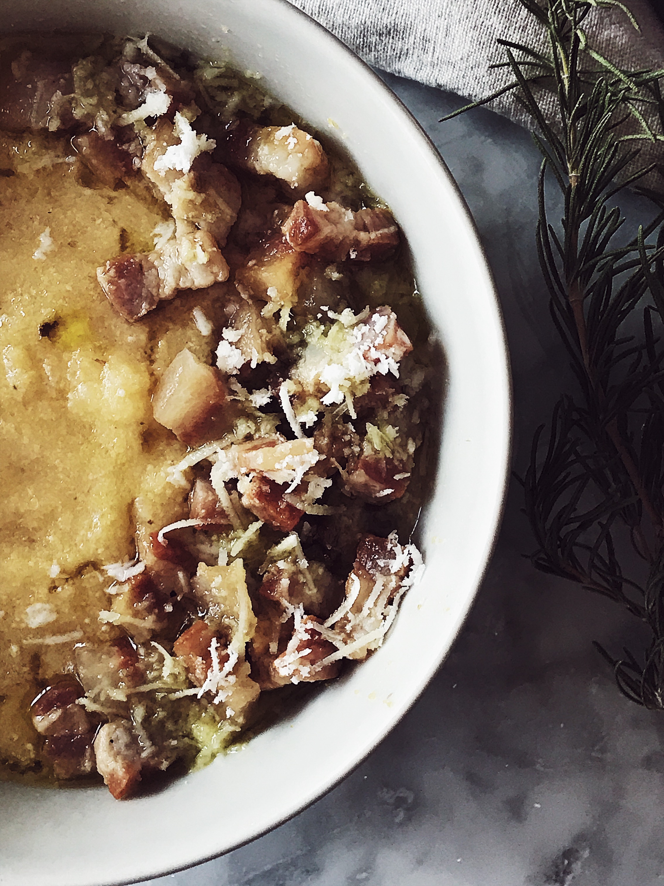 creamy polenta from cornmeal in a white bowl, seasoned with guanciale and grated pecorino cheese