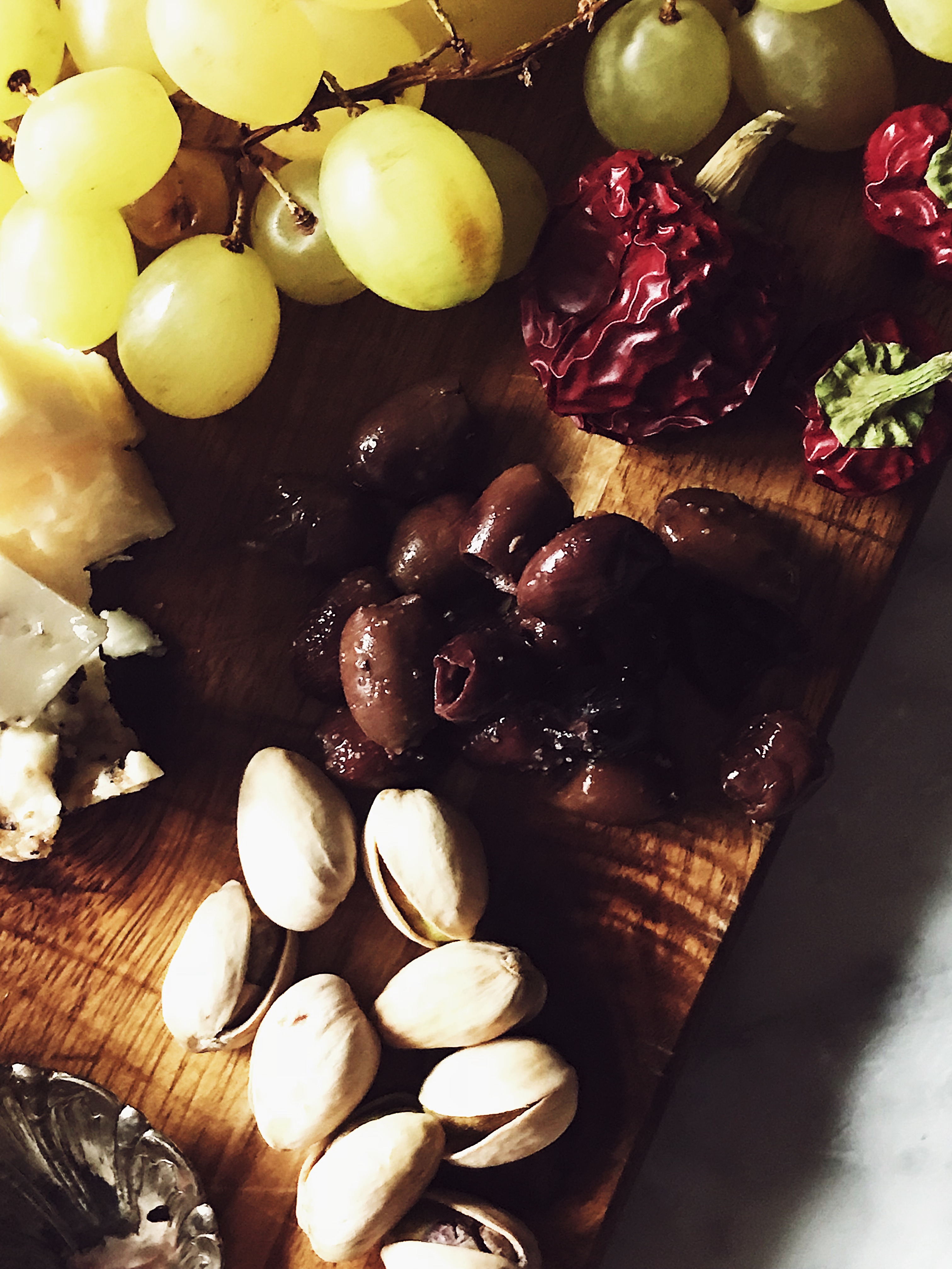 cheeses, grapes, olives, and pistachios on a wood cheese board