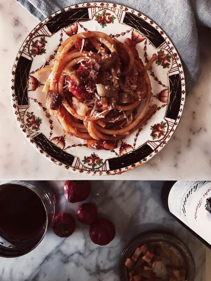 authentic amatriciana recipe on a fine china plate with a wine glass and bottle