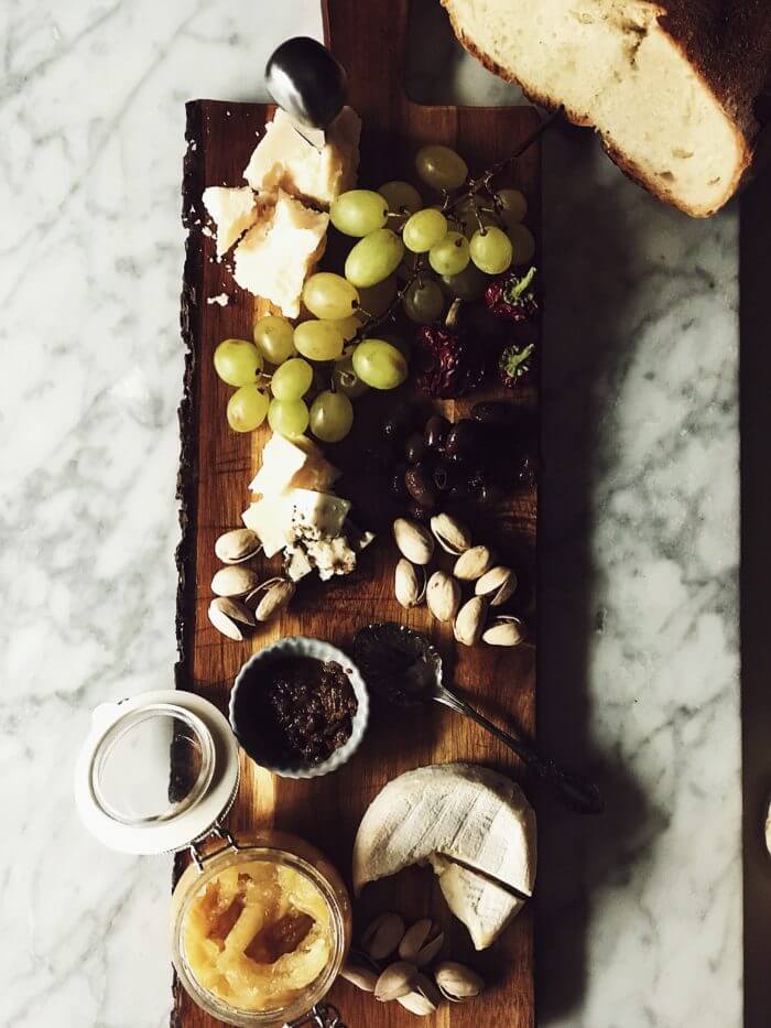 wooden cheese board with Italian cheeses, olives, pistachios, grapes, and Italian bread